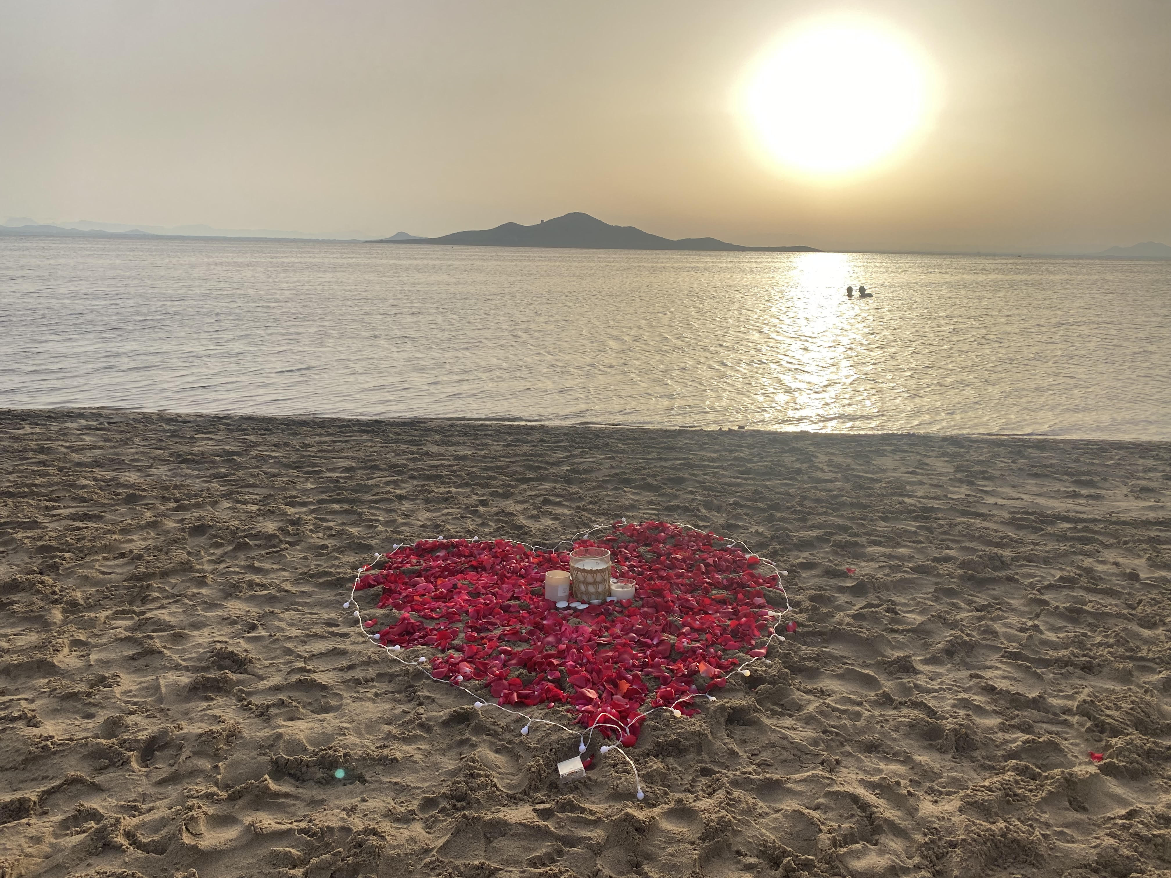 Un corazón hecho con una ritra de luces y pétalos de rosa en la playa